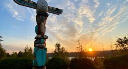 A Native American totem pole probably from the Pacific North West under a blue sky during the morning time. The Sun seems to be setting in the background. Photo by Ryan Stone on Unsplash